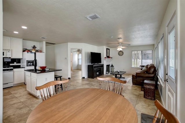 dining room featuring visible vents, baseboards, a fireplace, a textured ceiling, and a ceiling fan