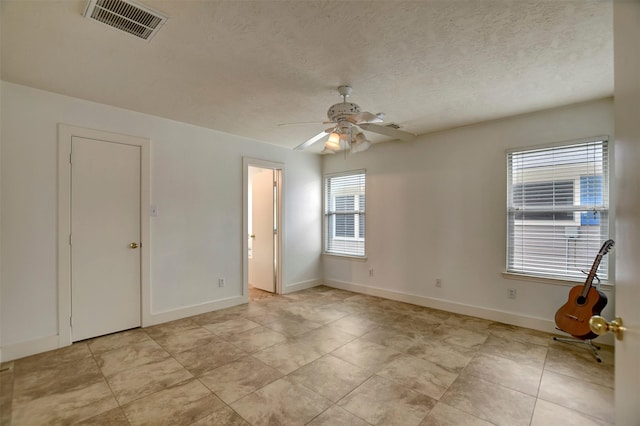 spare room with baseboards, visible vents, a textured ceiling, and ceiling fan