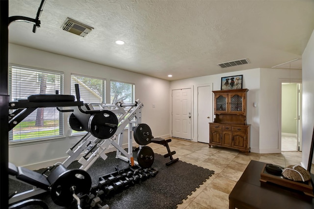 exercise area featuring visible vents, baseboards, a textured ceiling, and attic access