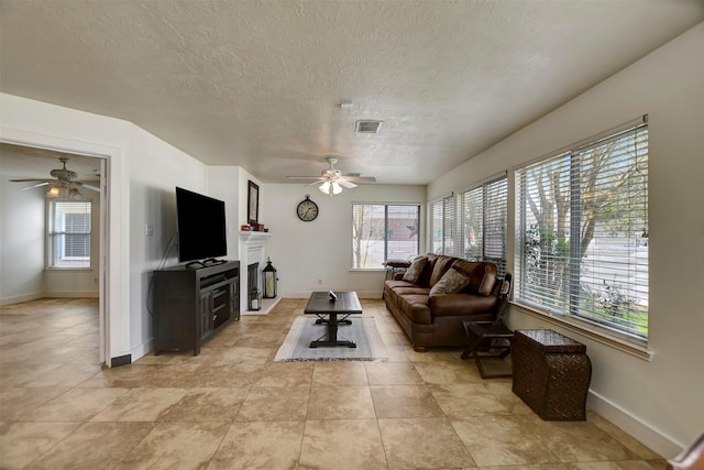 living room featuring baseboards, visible vents, a textured ceiling, and a ceiling fan