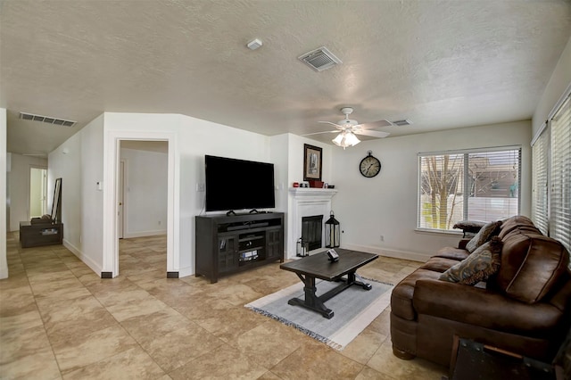 living area with visible vents, a fireplace, a textured ceiling, and ceiling fan