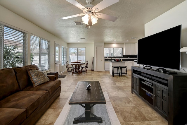 living room featuring visible vents, baseboards, a textured ceiling, and a ceiling fan