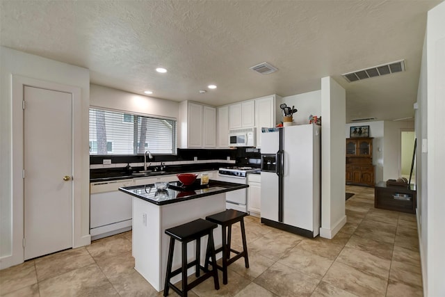 kitchen with white cabinetry, white appliances, visible vents, and a sink