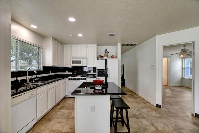 kitchen with visible vents, a sink, dark countertops, a kitchen island, and white appliances