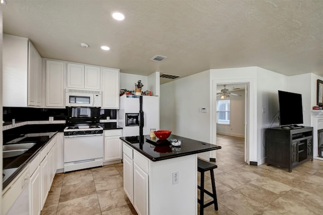 kitchen featuring visible vents, white cabinets, white appliances, and a breakfast bar