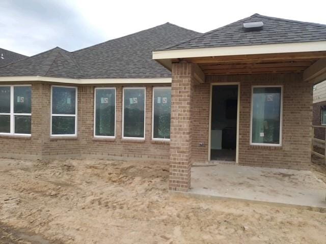 property entrance with a patio area, brick siding, and a shingled roof