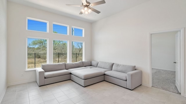 living area with light tile patterned floors, a ceiling fan, baseboards, and a towering ceiling