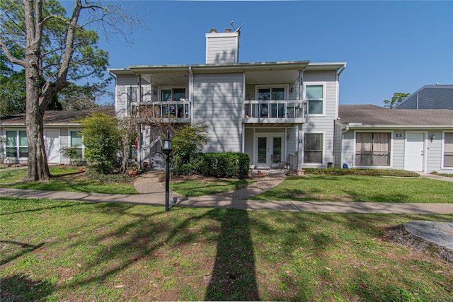 view of front of house featuring a chimney, french doors, a front yard, and a balcony