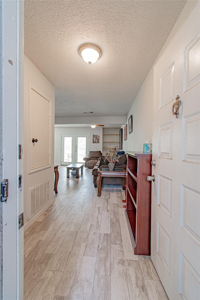 hallway with visible vents, a textured ceiling, and light wood finished floors