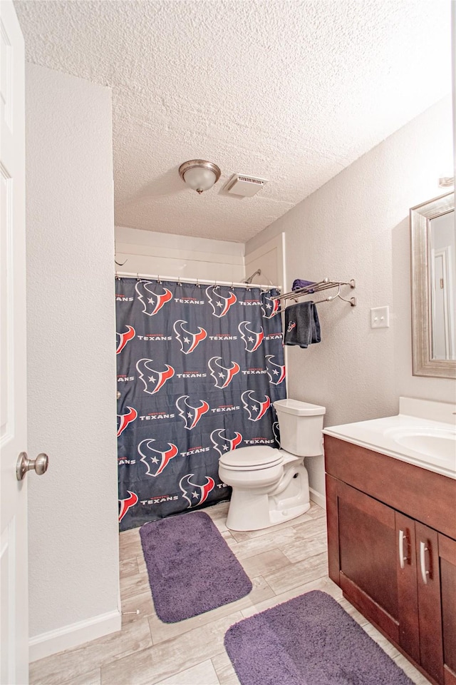 bathroom with visible vents, toilet, vanity, a textured wall, and a textured ceiling