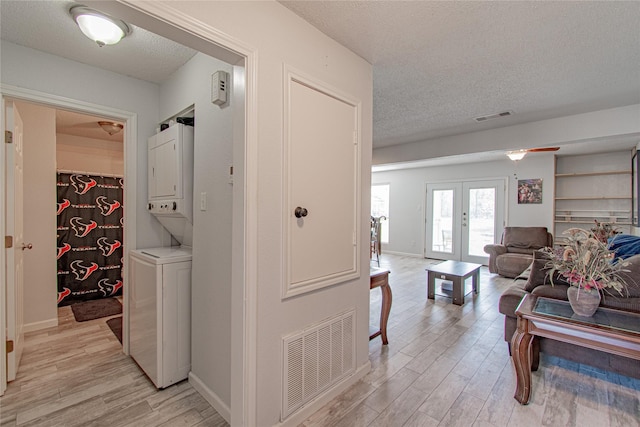 hall with light wood-style floors, stacked washer and dryer, french doors, and visible vents