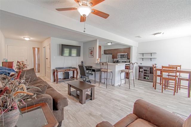 living room featuring light wood finished floors, a textured ceiling, and a ceiling fan