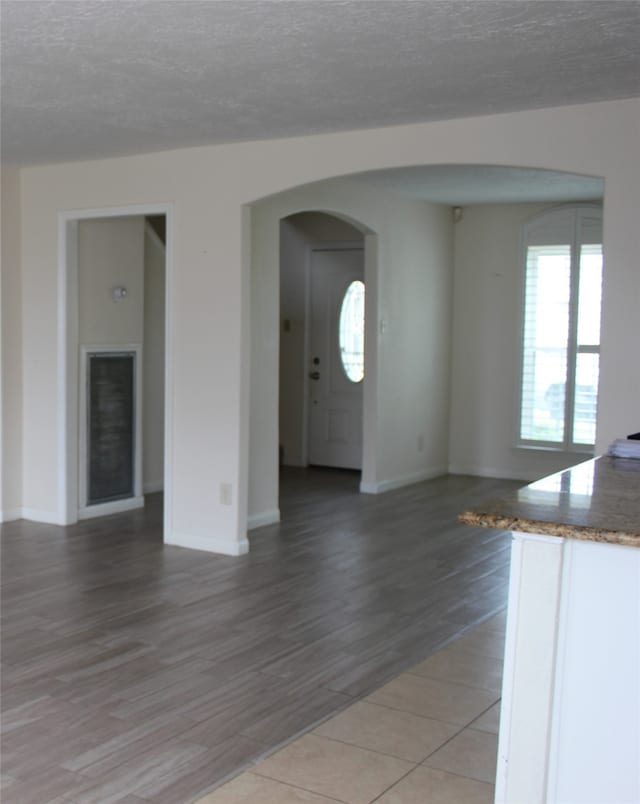 unfurnished living room with light wood-style flooring, baseboards, arched walkways, and a textured ceiling