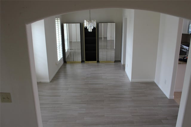 unfurnished dining area featuring light wood-style flooring, a notable chandelier, baseboards, and arched walkways