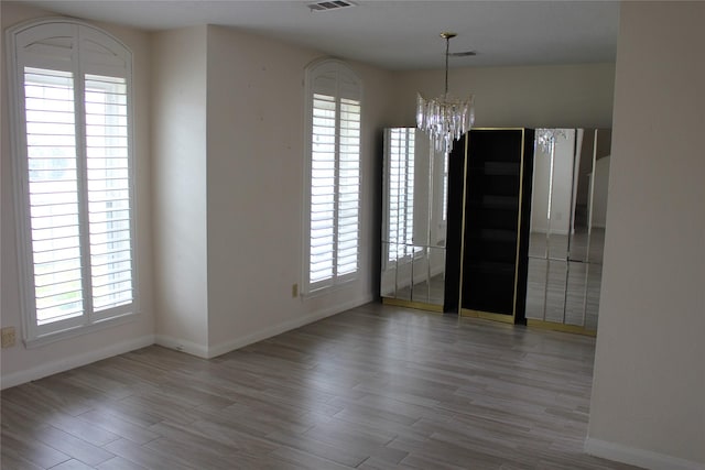 unfurnished dining area with a notable chandelier, wood finished floors, visible vents, and baseboards