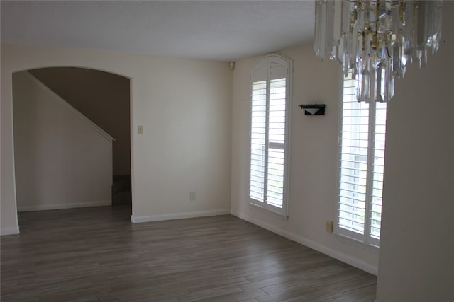 spare room with baseboards, arched walkways, and wood finished floors