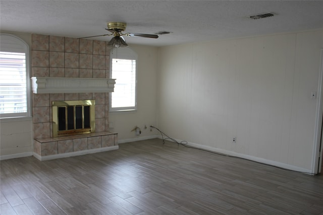 unfurnished living room with visible vents, a textured ceiling, wood finished floors, and a tile fireplace