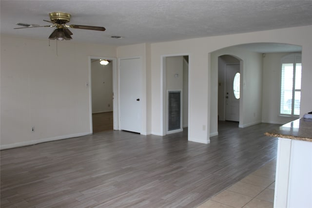 unfurnished living room featuring baseboards, ceiling fan, light wood-type flooring, arched walkways, and a textured ceiling