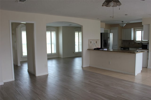 kitchen with arched walkways, backsplash, white cabinets, and stainless steel refrigerator with ice dispenser