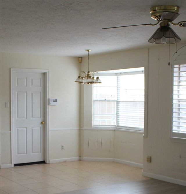 unfurnished dining area featuring ceiling fan with notable chandelier, baseboards, and a textured ceiling