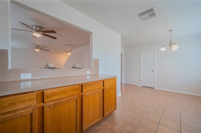 kitchen with visible vents, light tile patterned flooring, light countertops, pendant lighting, and brown cabinets