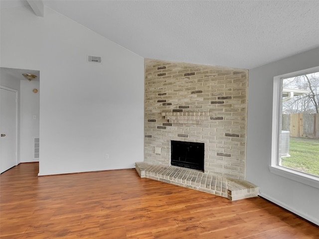 unfurnished living room featuring lofted ceiling, wood finished floors, a fireplace, and visible vents