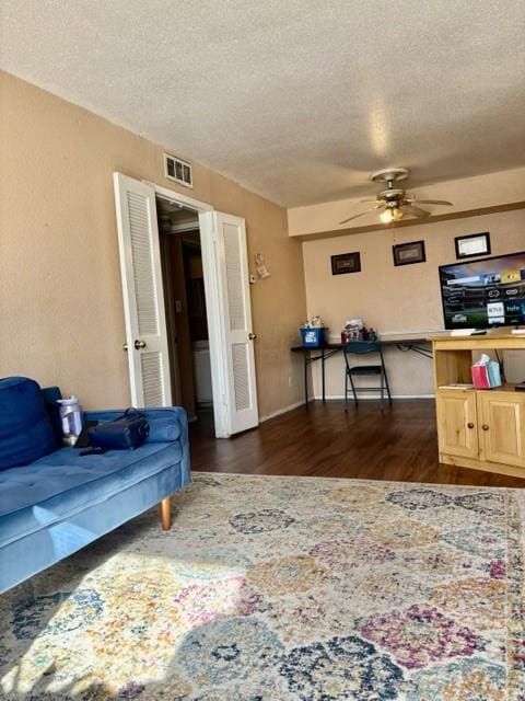 living area with a ceiling fan, dark wood-style floors, visible vents, and a textured ceiling