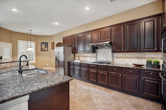 kitchen with stainless steel appliances, a sink, under cabinet range hood, decorative light fixtures, and backsplash