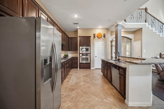 kitchen with a sink, dark stone countertops, tasteful backsplash, appliances with stainless steel finishes, and light tile patterned floors