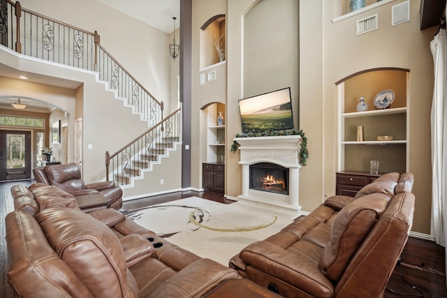 living area featuring visible vents, dark wood-type flooring, baseboards, built in features, and a lit fireplace