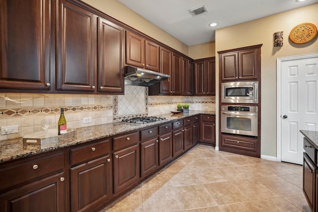 kitchen featuring under cabinet range hood, stainless steel appliances, visible vents, and decorative backsplash