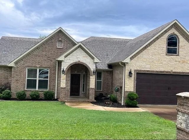 view of front of home featuring brick siding, a front yard, and a shingled roof