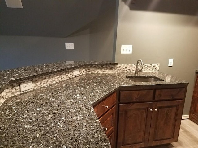 kitchen with a sink, dark stone counters, light wood-style floors, and backsplash