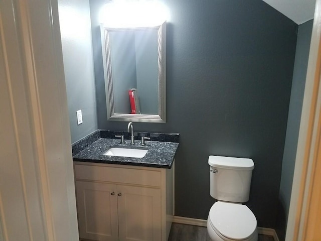 half bathroom featuring baseboards, toilet, wood finished floors, and vanity