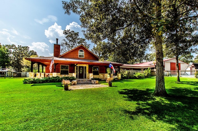 rear view of house featuring stone siding, a lawn, a chimney, and fence