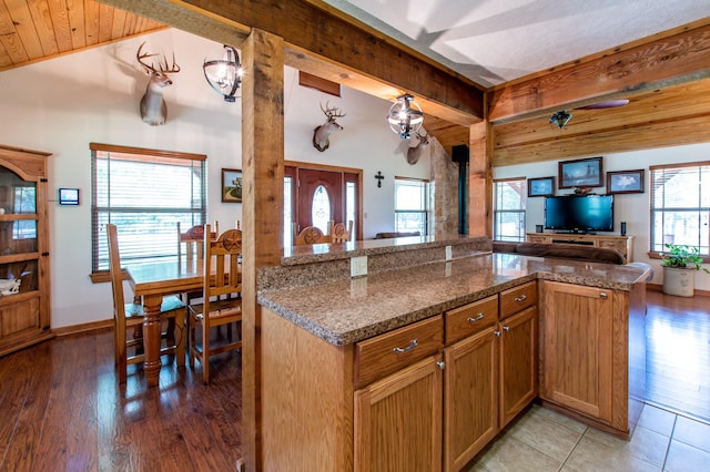 kitchen featuring light wood finished floors, vaulted ceiling with beams, open floor plan, a wood stove, and brown cabinetry