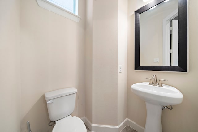 half bath featuring baseboards and toilet