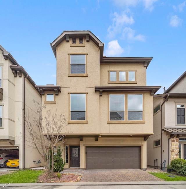 view of front of house featuring stucco siding, an attached garage, and decorative driveway