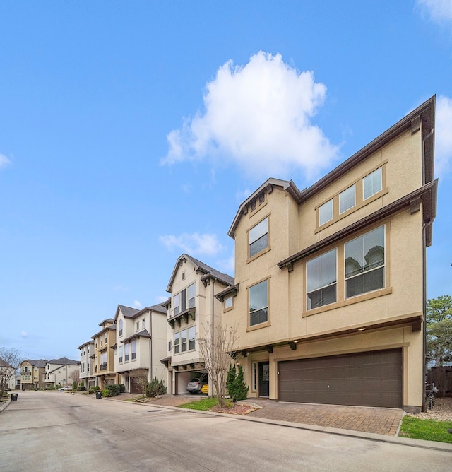 exterior space with stucco siding, a residential view, an attached garage, and decorative driveway