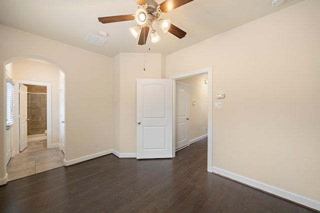 empty room featuring a ceiling fan, wood finished floors, arched walkways, and baseboards