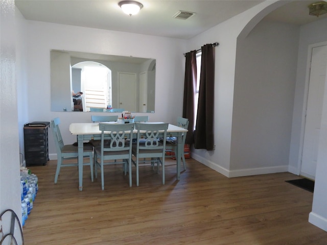 dining room featuring wood finished floors, arched walkways, visible vents, and baseboards