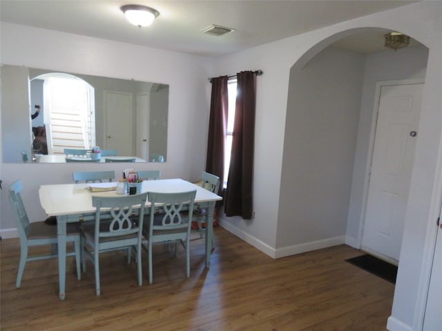 dining space featuring visible vents, baseboards, arched walkways, and wood finished floors