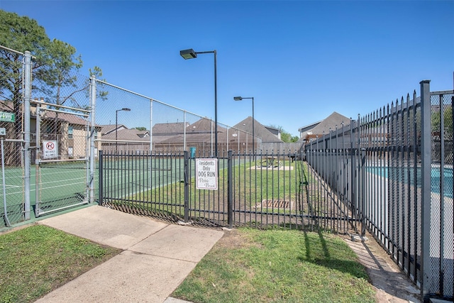 exterior space with a gate, a residential view, a tennis court, and fence