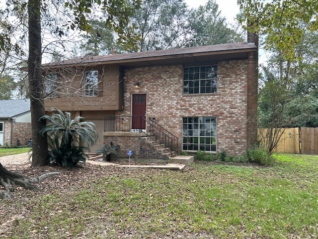 split foyer home with brick siding, a chimney, a front yard, and fence