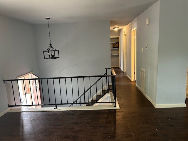 hallway with wood finished floors, an upstairs landing, baseboards, and a chandelier