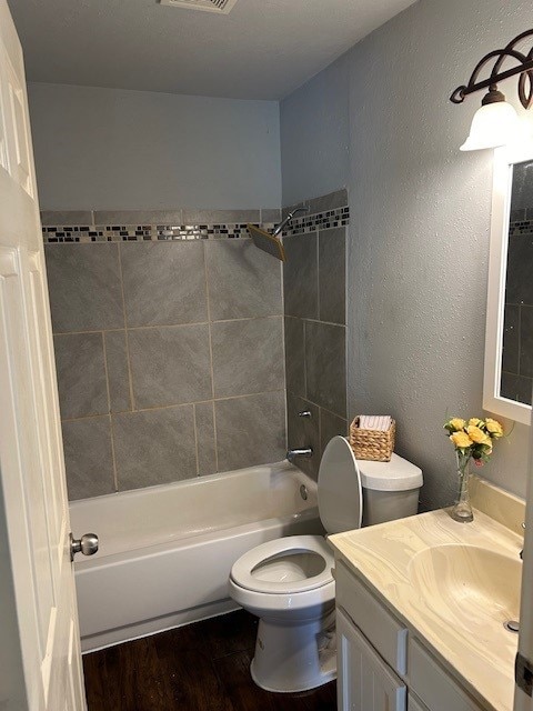 full bath with vanity, wood finished floors, bathtub / shower combination, toilet, and a textured wall