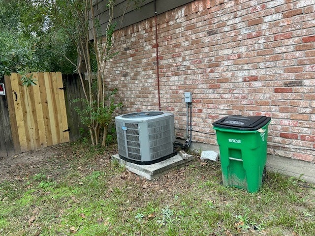 details featuring brick siding, central AC unit, and fence