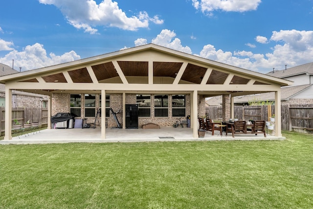 back of property featuring fence, a patio area, brick siding, and a lawn