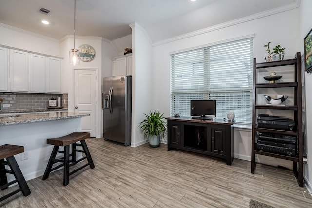 kitchen featuring a kitchen breakfast bar, tasteful backsplash, white cabinets, stainless steel fridge with ice dispenser, and light wood finished floors