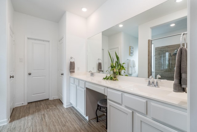 full bath featuring double vanity, wood finished floors, tiled shower, and a sink